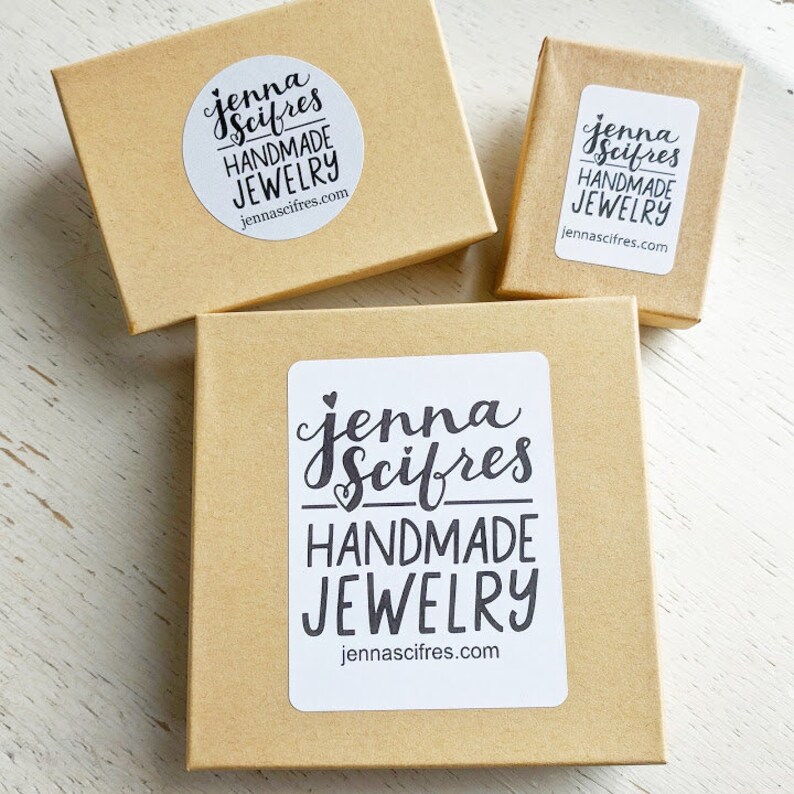 May include: Three brown cardboard boxes with a white sticker on each. The sticker has the text "Jenna Scires Handmade Jewelry" and the website address "jennascifres.com".