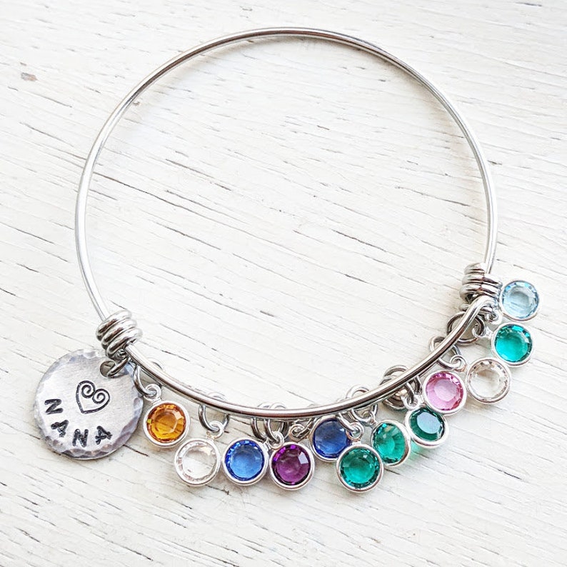 May include: A silver bangle bracelet with a charm that says "NANA" with a heart. The bracelet has multiple dangling charms with colorful crystals.