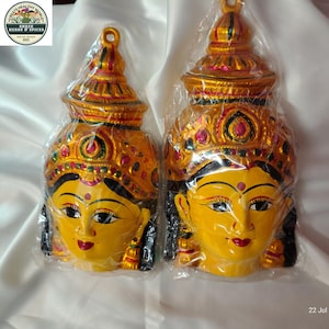 Può includere: Due maschere decorative da parete con volti gialli, capelli neri, segni bindi rossi e labbra rosse. Ogni maschera è decorata con una corona dorata ornata con dettagli rossi e verdi. Gli articoli sono confezionati singolarmente in plastica.