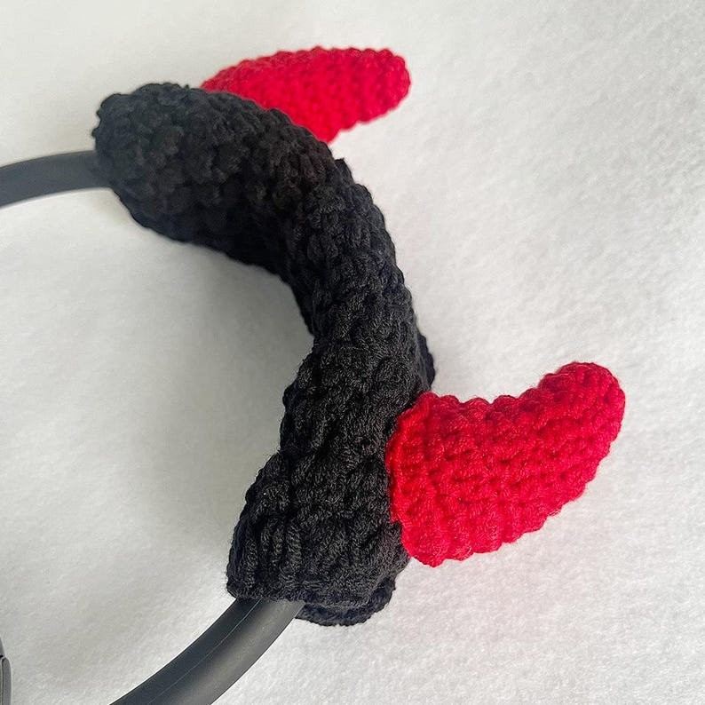 K&ouml;nnte beinhalten: Ein schwarzes geh&auml;keltes Stirnband mit zwei roten geh&auml;kelten H&ouml;rnern. Die herzf&ouml;rmigen H&ouml;rner sind an dem schwarzen Stirnband befestigt. Ein lustiges Accessoire f&uuml;r Kost&uuml;me oder Themenveranstaltungen.