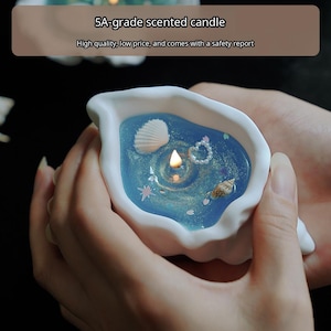 May include: A white shell-shaped container holding a blue scented candle with a lit wick. The wax surface is decorated with small seashells, a pearl heart, and star-shaped accents. Text on the image reads 5A-grade scented candle.