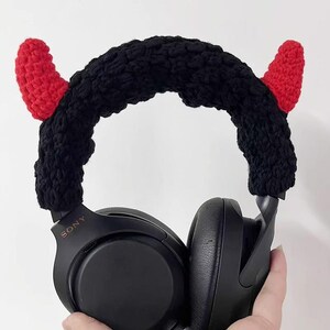 K&ouml;nnte beinhalten: Schwarzer Kopfh&ouml;rer mit einem geh&auml;kelten Teufelshorn-Stirnband. Das Stirnband ist schwarz mit zwei roten H&ouml;rnern. Der Kopfh&ouml;rer ist schwarz und tr&auml;gt den Markennamen "SONY". Das Stirnband ist so konzipiert, dass es &uuml;ber den Kopfh&ouml;rer passt.