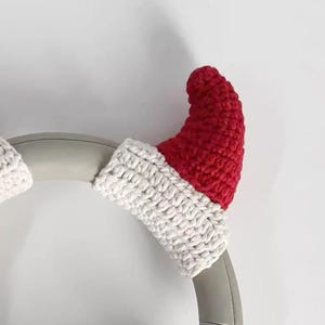 May include: A pair of red and white crocheted Santa hat covers for headphones. The red hat portion is crocheted, and the brim is white. The covers are designed to fit over the earcups of headphones, adding a festive touch.