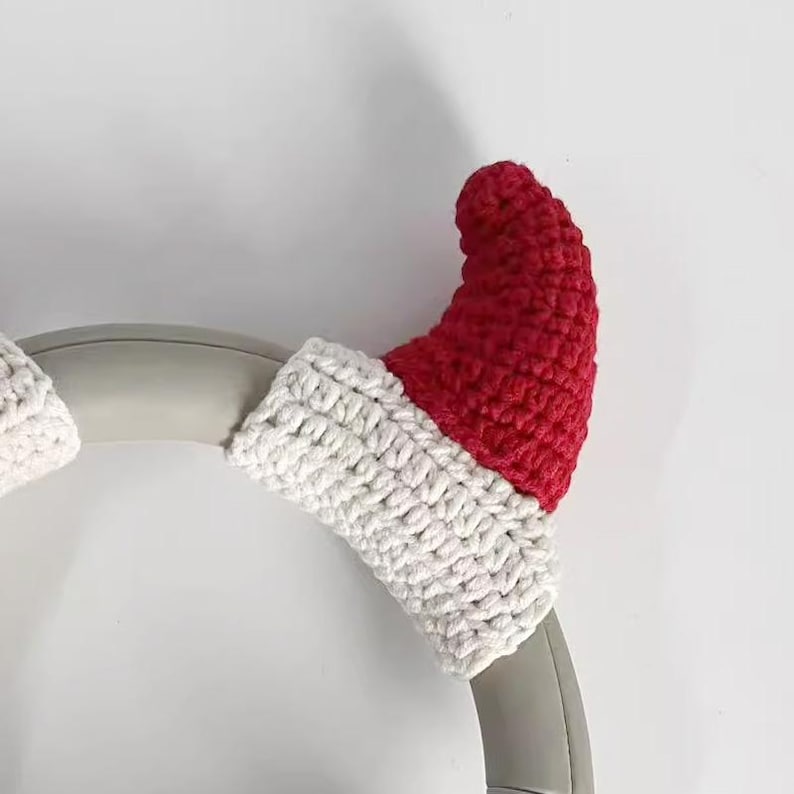May include: A pair of red and white crocheted Santa hat covers for headphones. The red hat portion is crocheted, and the brim is white. The covers are designed to fit over the earcups of headphones, adding a festive touch.