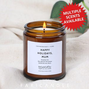 Può includere: Un barattolo di candela in vetro marrone acceso con un'etichetta bianca che recita "HAPPY HOLIDAYS, MUM". La candela è etichettata "COSY WINTER NIGHT - 42 HRS" e "SCENT-BLUE WIND CHIME". Un grafico a stella rossa indica che sono disponibili più profumi.