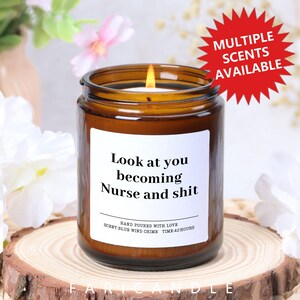 Op de afbeelding: Een bruine glazen potkaars met een brandende lont. Het etiket luidt "Look at you becoming Nurse and shit". De kaars staat op een houten schijf, met tekst die een blauwe windgonggeur en een brandtijd van 42 uur aangeeft.