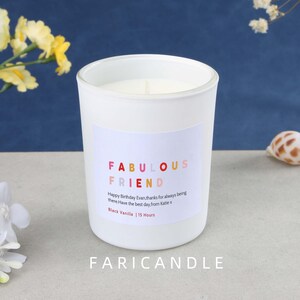 May include: A white glass candle with a label that reads "FABULOUS FRIEND" in colorful text. The label also includes a birthday message and scent information. The candle is labeled "Black Vanilla | 15 Hours". The brand name "FARICANDLE" is at the bottom.
