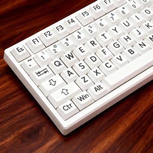 May include: A white computer keyboard with black lettering, set against a dark wood grain surface. The keys include letters, numbers, and function keys. The keyboard is a standard QWERTY layout.