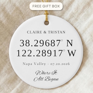 Peut inclure: Un ornement rond en céramique blanche avec du texte noir indiquant CLAIRE & TRISTAN, les coordonnées 38.29687 N 122.28917 W, Napa Valley - 07.20.2026, et la phrase Where It All Began. Une ficelle dorée est fixée par un trou au sommet.