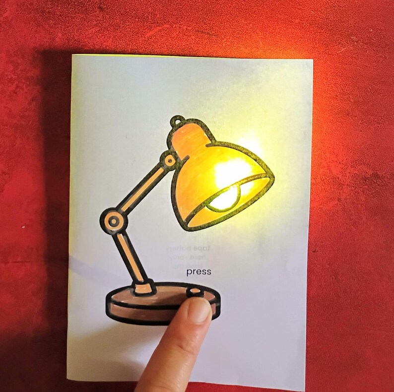 May include: A drawing of a desk lamp with a glowing yellow light on a white background. The lamp is orange and brown, with the word "press" below a button. A finger is pressing the button.