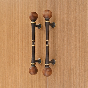 May include: Two cabinet door handles with a dark bronze finish and wooden spheres at each end. The handles have a decorative gold accent and are mounted on a light wood cabinet door.