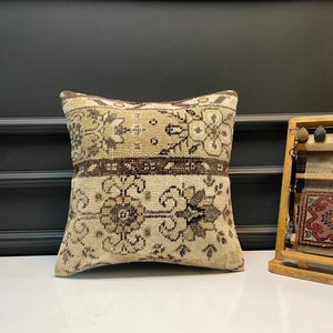 Könnte beinhalten: Ein quadratisches Kissen mit beigem und braunem Blumenmuster. Das Kissen hat einen Vintage-Look mit hellen und dunklen Brauntönen. Es besteht wahrscheinlich aus einem gewebten Material und ist ein dekoratives Wohnaccessoire.