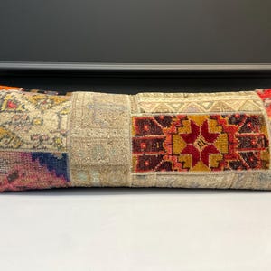 Peut inclure: Coussin rectangulaire en patchwork avec une variété de couleurs et de motifs. Il présente des sections de tissus beiges, rouges, oranges et bleus. Le design comprend des motifs géométriques et floraux, créant un aspect unique et texturé. Le coussin est décoratif.