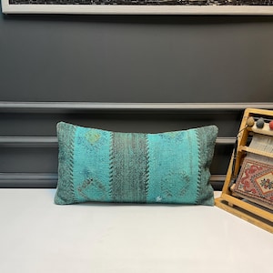 May include: Rectangular turquoise pillow with a patchwork design. The pillow features vertical stripes in varying shades of teal and green. The pillow is made of a textured fabric.