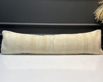 May include: Cream-colored lumbar pillow with a rectangular shape. The pillow has a textured surface with vertical stripes. The pillow is placed on a white surface with a dark background.