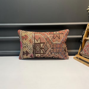 May include: Rectangular decorative pillow with a woven, patterned design in shades of red, brown, and beige. The pillow features a geometric pattern with a vintage, distressed look, adding a touch of rustic charm to any space.