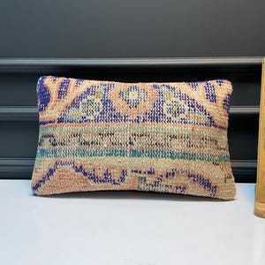 May include: Rectangular cushion with a woven, textured design. The cushion features a pattern with blue, peach, and beige colours. The cushion is a decorative item, likely for a sofa or bed.