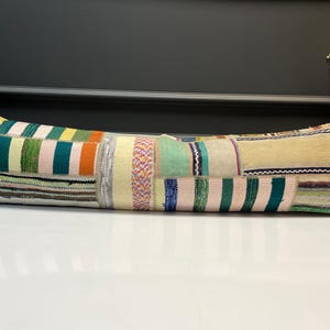 Könnte beinhalten: Ein langes, rechteckiges Kissen mit einem Patchwork-Design. Das Kissen hat eine Vielzahl von Farben, darunter Grün, Rosa, Orange und Gelb. Das Kissen liegt auf einer weißen Oberfläche.