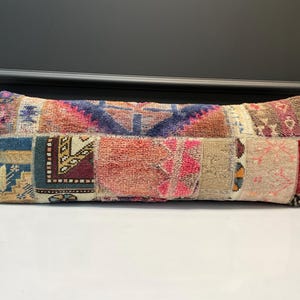 May include: Rectangular patchwork pillow with a variety of colors and patterns. The pillow features a mix of textures and designs, including geometric shapes, floral motifs, and a range of colors such as blue, red, beige, and brown. The pillow is designed for decorative use.