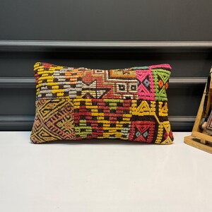 Peut inclure: Coussin rectangulaire décoratif avec un motif patchwork. Le coussin présente un mélange de couleurs vives, notamment le jaune, le rouge, le vert et le rose. Le design intègre des motifs et des formes géométriques.