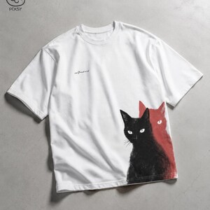 May include: A white short-sleeve t-shirt featuring a graphic of a black cat in the foreground and a red cat silhouette behind it. The shirt includes the word selfaware printed in small black cursive script on the upper right chest area.
