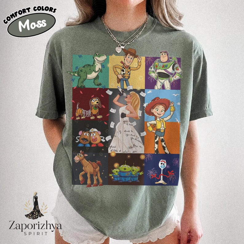 May include: A moss green short-sleeve t-shirt featuring a grid of nine colorful illustrations of animated characters, including a green dinosaur, a cowboy, a space ranger, a dog, a blonde singer, a cowgirl, potato figures, a horse, aliens, and a fork.