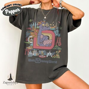 May include: Dark grey t-shirt with a colourful graphic of a purple dragon character inside a large letter "D" with a rainbow. The shirt also includes the text "Walt Disney World" and the Comfort Colors and Zaporizhya Spirit logos.