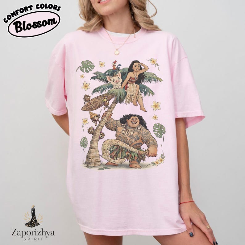 Może przedstawiać: Jasnor&oacute;żowa koszulka z kolorową ilustracją postaci z popularnego filmu animowanego. Projekt zawiera palmę, kwiaty i napis "Comfort Colors Blossom". Koszulka ma luźny kr&oacute;j.