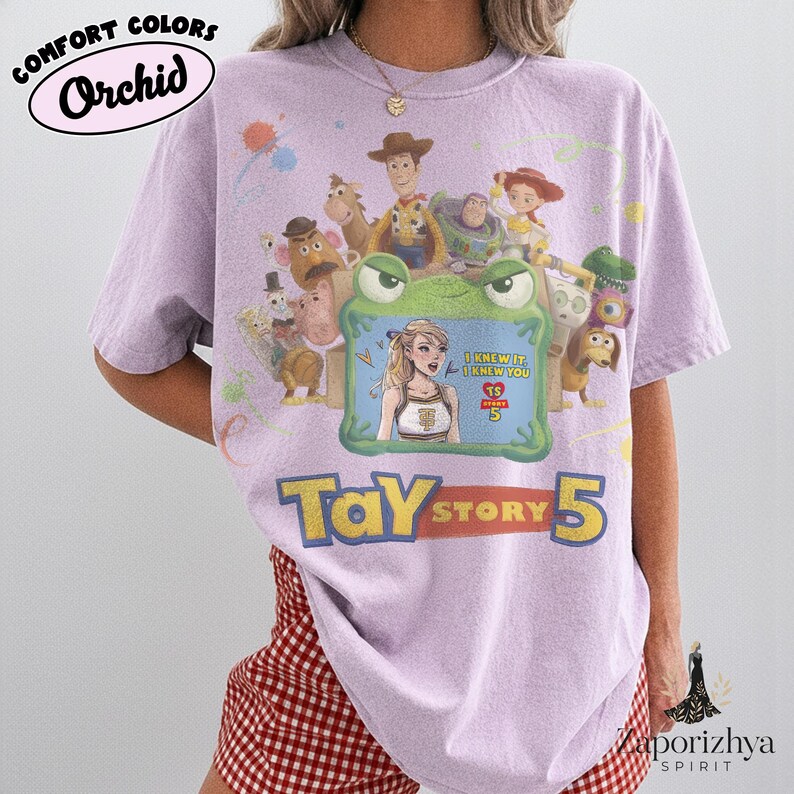 May include: A light purple short-sleeve t-shirt featuring a graphic print of Toy Story characters surrounding a green frog-shaped frame. Inside the frame is an illustration of a blonde person with the text I KNEW IT I KNEW YOU TS STORY 5.