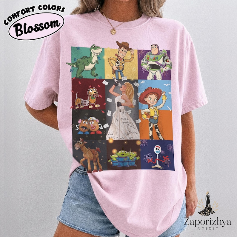 May include: A light pink t-shirt featuring a grid of nine panels displaying various animated characters, including a cowboy, a space ranger, a cowgirl, a dinosaur, a dog, a horse, potato figures, aliens, and a spork, with a central figure singing.