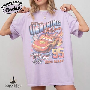 May include: A light purple t-shirt featuring a graphic of Lightning McQueen from the movie Cars. The design includes the text "Street Legend Lightning McQueen", "Need for Speed", and "Race Ready", with the number "95". The shirt has the "Comfort Colors" and "Orchid" logos.