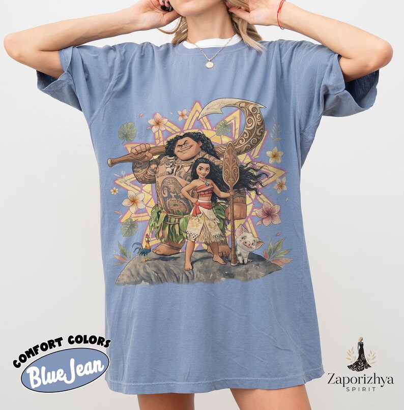 May include: Blue jean Comfort Colors t-shirt featuring a colorful graphic of characters from a popular animated movie. The design includes a large figure with tattoos, a young woman, a pig, and a rooster. The shirt has the words "Comfort Colors" and "Blue Jean" printed on it.