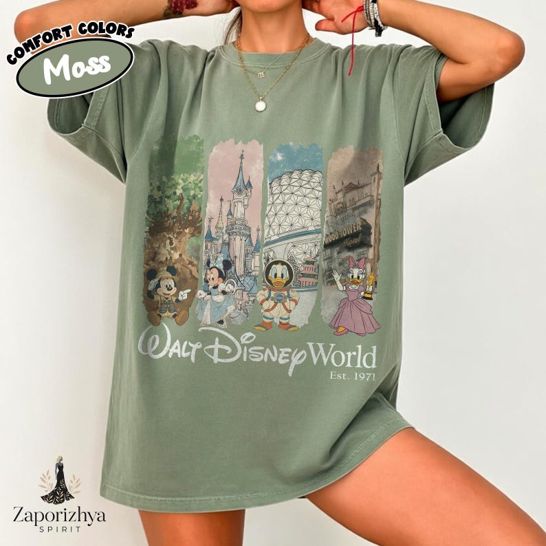 May include: A moss green t-shirt with a vibrant graphic showcasing Walt Disney World characters and landmarks. The design includes Mickey, Minnie, Donald, and Daisy Duck. The text "Walt Disney World Est. 1971" is printed below the graphic.
