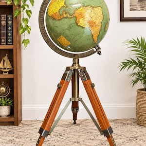 Puede incluir: Un globo terráqueo de pie con un mapa verde y amarillo de las Américas, montado sobre un anillo meridiano de latón. El globo se apoya en un trípode de madera de tres patas con herrajes de latón y soportes metálicos ajustables.