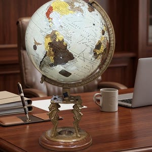 Op de afbeelding: Een verlichte wereldbol in vintage-stijl met een gedetailleerde wereldkaart. De bol staat op een decoratieve messing standaard met een houten voet. De bol is van binnenuit verlicht, waardoor de continenten en oceanen worden benadrukt. Een pen, notitieblok en koffiemok staan op het bureau. De diameter is ongeveer 30 cm.
