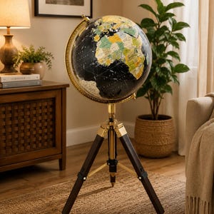 Puede incluir: Un globo terráqueo de pie con océanos negros y continentes multicolores. La esfera está montada sobre un meridiano dorado y se sostiene mediante un trípode compuesto por patas de madera oscura con detalles metálicos en tono dorado.