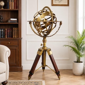 May include: A floor-standing armillary sphere featuring a series of interlocking brass rings and a central globe, mounted on a tripod base constructed from dark wood with brass accents and pointed metal feet, standing on a wooden floor.
