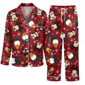 Può includere: Un set di pigiama rosso composto da una camicia a maniche lunghe con bottoni e pantaloni abbinati, caratterizzato da un motivo ripetuto di personaggi Disney come Topolino, Minnie, Paperino e Pluto con cappelli natalizi e fiocchi di neve.