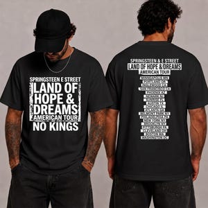 May include: A black short-sleeved t-shirt featuring white graphic text. The front displays 'SPRINGSTEEN E STREET LAND OF HOPE & DREAMS AMERICAN TOUR NO KINGS'. The back lists various American tour cities including Minneapolis, Portland, and Washington DC.