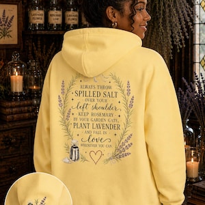 May include: A pale yellow hooded sweatshirt featuring a back graphic with lavender sprigs, a lantern, and the text: ALWAYS THROW SPILLED SALT OVER YOUR LEFT SHOULDER, KEEP ROSEMARY BY YOUR GARDEN GATE, PLANT LAVENDER AND FALL IN LOVE WHENEVER YOU CAN.