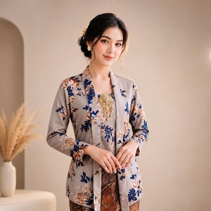 May include: A woman in a traditional outfit. The outfit features a grey jacket and top with a floral pattern in blue and brown. A gold brooch is on the top. The outfit is completed with a patterned skirt.