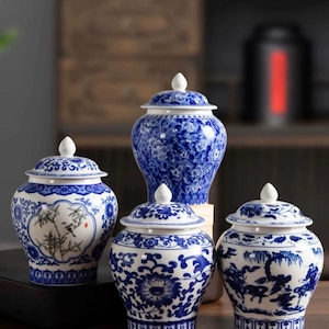May include: Four blue and white ceramic jars with lids. The jars feature intricate floral and landscape designs. The jars are of varying sizes and shapes, with white finials on the lids. The color scheme is a classic combination of blue and white.