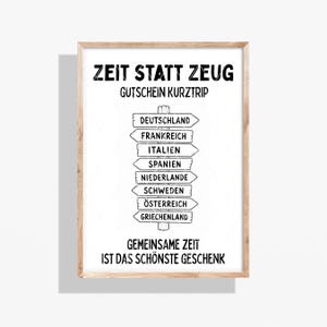 May include: A framed white poster featuring black text and a central signpost graphic. The text reads ZEIT STATT ZEUG, GUTSCHEIN KURZTRIP, and GEMEINSAME ZEIT IST DAS SCHÖNSTE GESCHENK. The signpost lists countries: DEUTSCHLAND, FRANKREICH, ITALIEN, SPANIEN, NIEDERLANDE, SCHWEDEN, ÖSTERREICH, GRIECHENLAND.