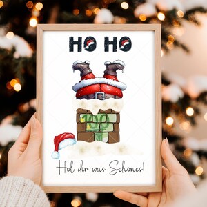 May include: A framed Christmas illustration showing Santa Claus stuck in a chimney, with his legs and boots visible. The image includes the text "HO HO" at the top and "Hol dir was Schones!" at the bottom. A Santa hat rests on the snow.