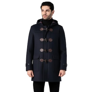 Può includere: Duffle coat blu navy con cappuccio e chiusure a toggle. Il cappotto presenta due tasche frontali e dettagli marroni effetto pelle. Il modello indossa pantaloni neri e scarpe marroni.