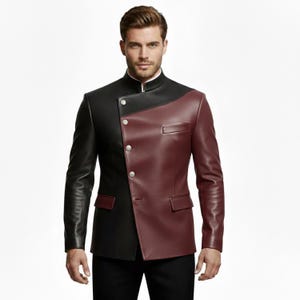 May include: A two-tone leather jacket in black and burgundy. The jacket features a mandarin collar, asymmetrical design, and silver buttons. The jacket has a tailored fit and a pocket on the burgundy side.