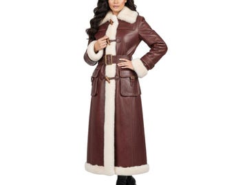 Könnte beinhalten: Langer, burgunderfarbener Ledermantel mit cremefarbenem Shearling-Besatz. Der Mantel hat einen Gürtel, Knebelverschlüsse und Taschen. Das Model trägt schwarze Stiefel. Die Mantellänge beträgt ca. 140 cm.