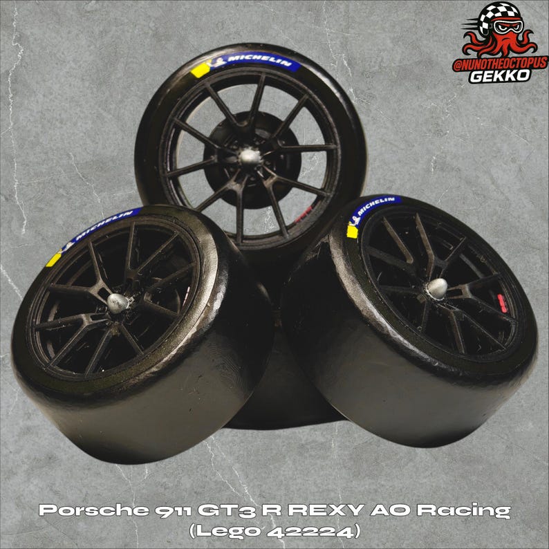 May include: Three black racing tires with black rims are stacked together. Each tire has a blue and yellow Michelin logo. The text "Porsche 911 GT3 R REXY AO Racing (Lego 42224)" is at the bottom of the image.