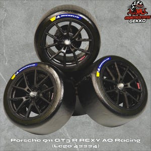 May include: Three black racing tires with Michelin branding and yellow accents. The tires are from a Porsche 911 GT3 R REXY AO Racing Lego set (42224). The wheels have a complex spoke design.