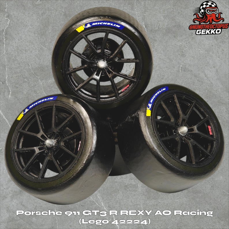 May include: Three black racing tires with Michelin branding and yellow accents. The tires are from a Porsche 911 GT3 R REXY AO Racing Lego set (42224). The wheels have a complex spoke design.